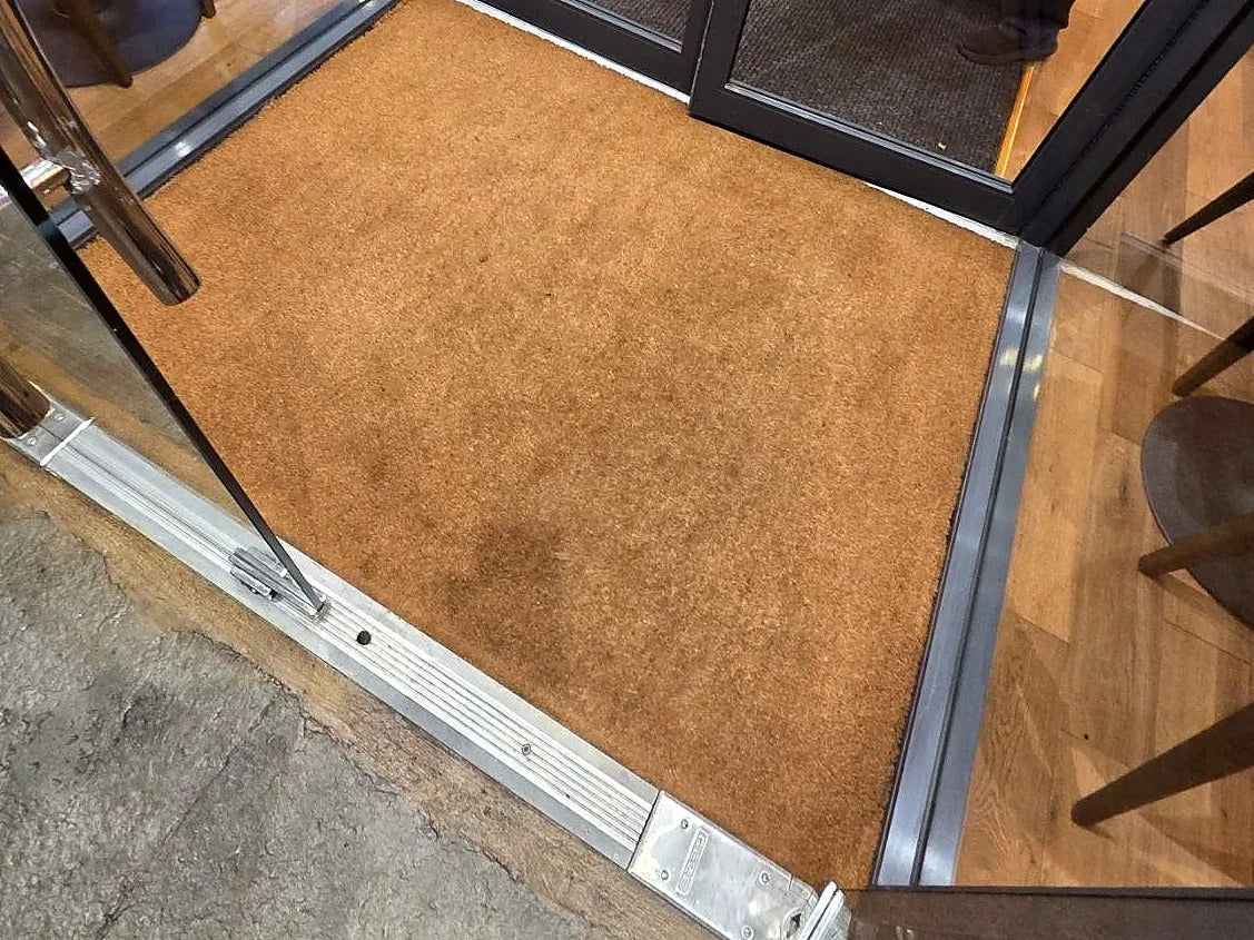 A natural coir mat set flush in a recessed well inside glass entrance doors